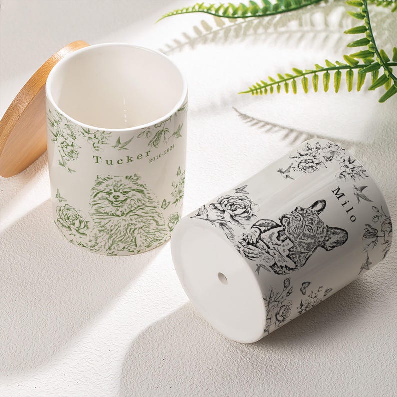 May include: Two white ceramic plant pots with floral and pet illustrations. One pot features a Pomeranian with the name "Tucker" and the years "2010-2024". The other pot displays a French Bulldog with the name "Milo".