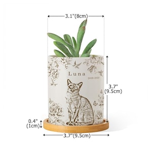 May include: A white ceramic planter, 3.7 inches (9.5 cm) tall and 3.1 inches (8 cm) wide, featuring a cat illustration and the name "Luna" with dates. The planter includes a small succulent and sits on a wooden saucer, 3.7 inches (9.5 cm) in diameter.