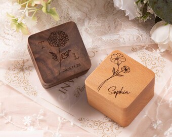 May include: Two wooden ring boxes with engraved floral designs. The box on the left has a flower and the date 2024.11.26 engraved on it. The box on the right has a flower and the name "Sophia" engraved on it.
