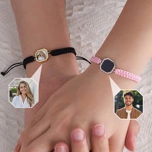 Puede incluir: Dos pulseras personalizadas a juego. Una es negra con un colgante octogonal dorado, la otra es rosa con un colgante octogonal plateado. Cada colgante presenta una foto. Las pulseras están conectadas al sostenerse de las manos.