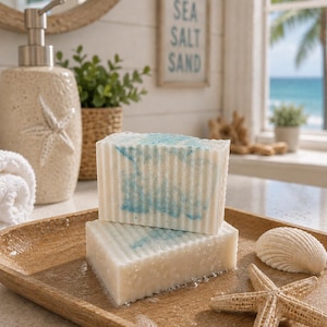 May include: Two rectangular bars of white soap with vertical ridges and blue marbled swirls. The soap is placed on a wooden tray alongside a white seashell and a tan starfish. The soap has a textured surface and appears slightly damp.