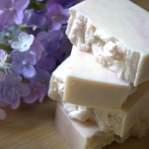 Può includere: Una pila di quattro saponette bianche e rosa con un motivo floreale. Le saponette sono disposte a forma di piramide.