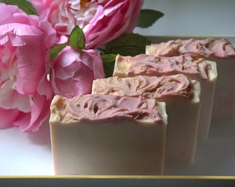 Op de afbeelding: Vier rechthoekige handgemaakte zeepblokken, crème van kleur met een roze wervelontwerp bovenop. De achtergrond toont roze pioenrozen. Elke zeep is ongeveer 8 cm lang.