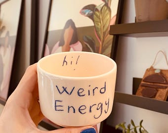 May include: White ceramic mug with blue lettering that reads "hi! Weird Energy".