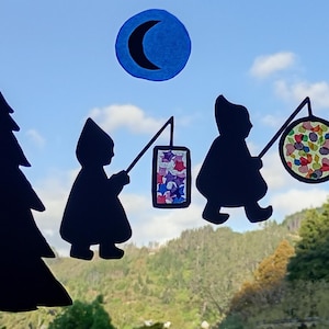Puede incluir: Recortes de siluetas de figuras que llevan linternas y caminan entre árboles de hoja perenne estilizados. Una luna creciente está en el cielo. Las linternas tienen diseños coloridos, incluyendo estrellas, confeti y hojas de otoño. El fondo es una vista de una cordillera.