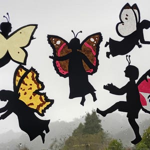 May include: Five whimsical butterfly cutouts in various colors and patterns are displayed against a cloudy background. The silhouettes feature human-like figures with butterfly wings, creating a playful and artistic scene. The wings have yellow, red, and white accents.