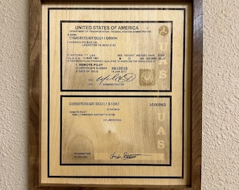 May include: A framed document from the United States of America, featuring text about a Remote Pilot. The document is in a wooden frame. The text includes the name, address, and certificate number. The document is a UAS certificate.