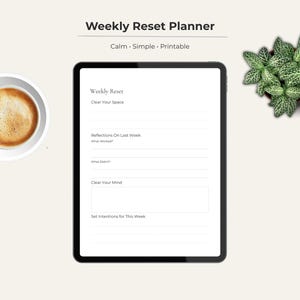 May include: A digital planner on a tablet with the text "Weekly Reset Planner." The tablet is black with a white screen displaying a planner layout. A cup of coffee and a small green plant are also in the image.