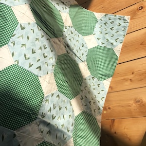 May include: A green and blue patchwork quilt with a floral pattern. The quilt is made of different fabrics and is sewn together in a hexagonal pattern.