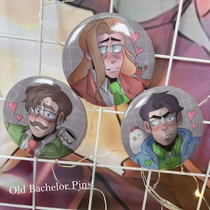 May include: Three round pins with cartoon illustrations of three men with different hairstyles and facial expressions. Each pin has a plaid background and pink hearts. The text "Old Bachelor Pins!" is visible at the bottom of the image.