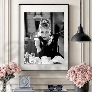 May include: A monochrome framed print featuring Audrey Hepburn in a black dress and pearls. The print is displayed above a shelf with pink roses, books, and sunglasses. A black pendant light hangs from the ceiling. The image evokes classic Hollywood glamour.