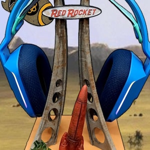 以下が含まれることがあります： ロケットのデザインが施された青とターコイズブルーのヘッドセットスタンド。スタンドには「Red Rocket」と書かれた看板があります。