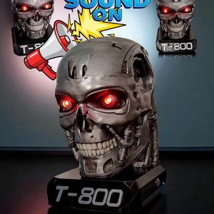 May include: A metallic silver T-800 skull with glowing red eyes, mounted on a black base. The base is labeled "T-800". The image includes the text "SOUND ON" with a megaphone graphic, and two additional skull figures.