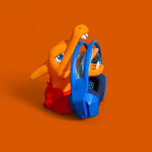 May include: Orange and red cartoon character holding a pair of blue headphones. The headphones have a blue and green design on the earcups.
