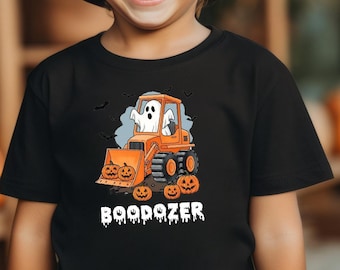 May include: A black t-shirt featuring a graphic of a white ghost driving an orange bulldozer with small jack-o'-lanterns around it. The text BOODOZER is printed in white below the graphic. The shirt is worn with a black hat.