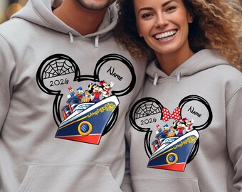 May include: Two light gray hooded sweatshirts featuring a graphic of a cruise ship inside a Mickey Mouse ear silhouette. The design includes the text 2026 and a placeholder for a name, with cartoon characters on the ship deck and a spiderweb detail.