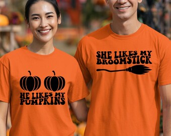 May include: Two orange short-sleeve t-shirts with black graphic text and illustrations. One shirt features two pumpkin icons and the text HE LIKES MY PUMPKINS. The other shirt features a broomstick icon and the text SHE LIKES MY BROOMSTICK.