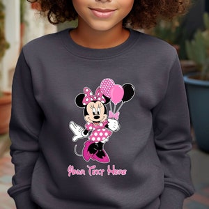 Puede incluir: Una sudadera gris con un gr&aacute;fico rosa de Minnie Mouse sosteniendo globos rosas. El texto "Your Text Here" est&aacute; impreso debajo del gr&aacute;fico.
