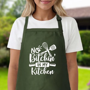 May include: A green apron with white text that says "No Bitchin' in my Kitchen" and a white graphic of a whisk and spatula.