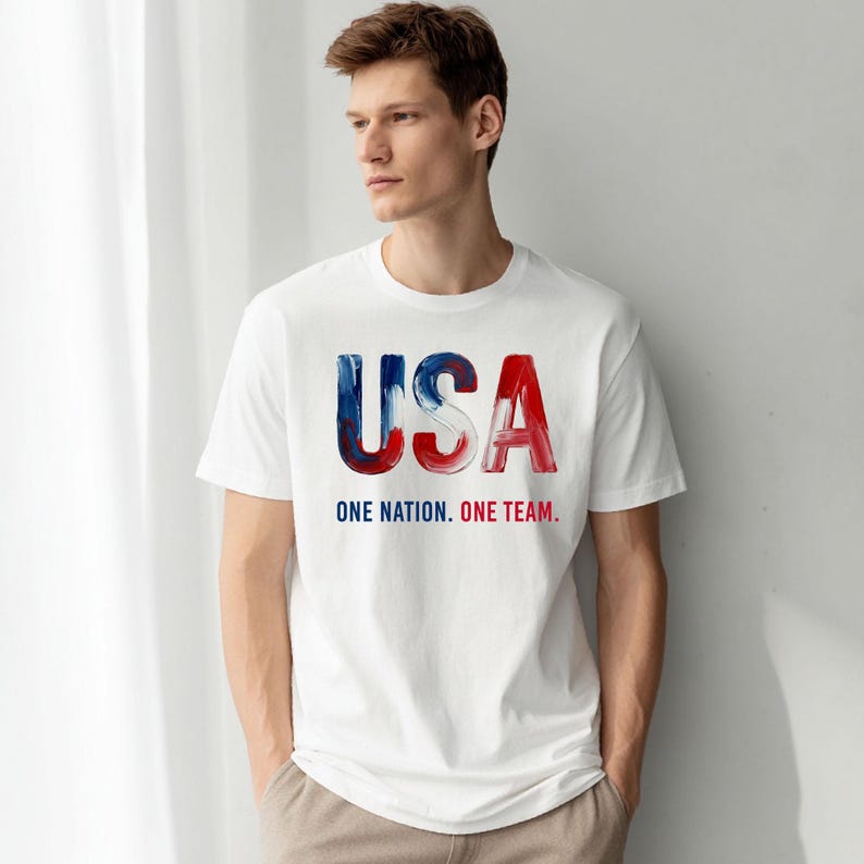 K&ouml;nnte beinhalten: Wei&szlig;es T-Shirt mit dem Wort "USA" in rot, wei&szlig; und blau. Unter dem Wort "USA" steht der Text "ONE NATION. ONE TEAM."