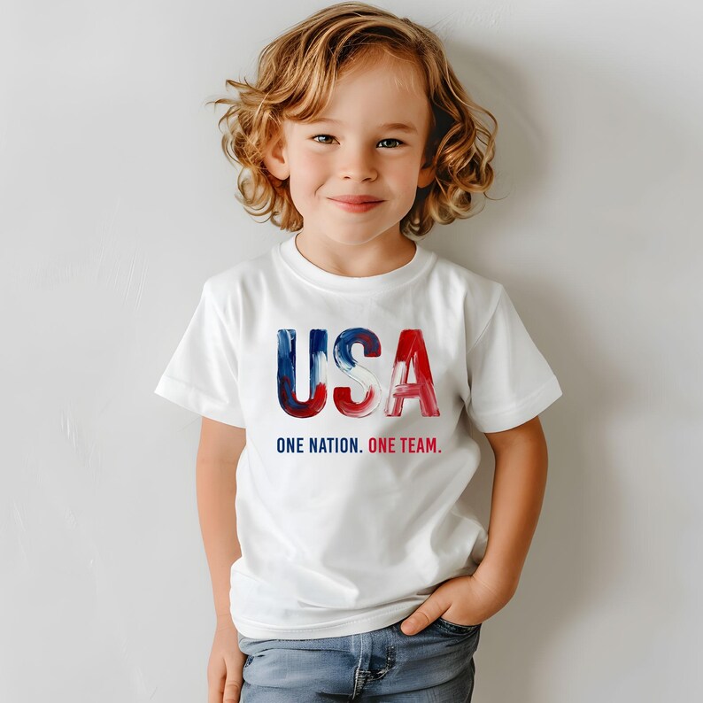 K&ouml;nnte beinhalten: Wei&szlig;es T-Shirt mit dem Wort "USA" in blau-roter Aquarellschrift. Unter dem Wort "USA" steht der Text "ONE NATION. ONE TEAM."