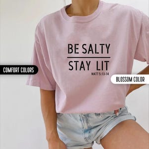 May include: A pink t-shirt with the text "BE SALTY STAY LIT" and the scripture reference "MATT 5:13-14" printed in black.