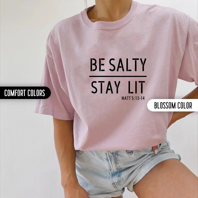May include: A pink t-shirt with the text "BE SALTY STAY LIT" and the scripture reference "MATT 5:13-14" printed in black.