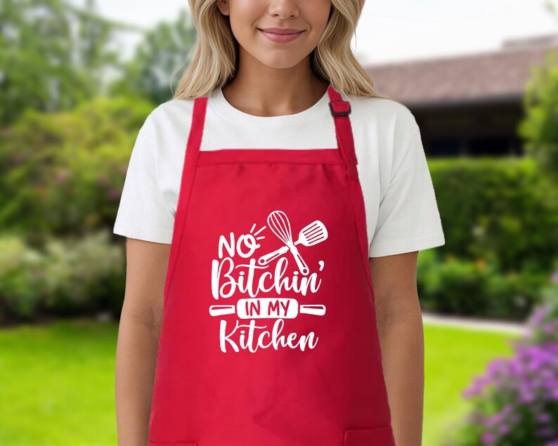 May include: Red kitchen apron with white text that says "No Bitchin' in my Kitchen" and a white whisk and spatula graphic.