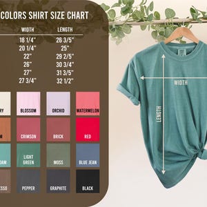 May include: A teal Comfort Colors t-shirt hanging on a wooden hanger, with a size chart and color swatches to the left. The chart lists shirt sizes and measurements in inches, including width and length. Colors include white, ivory, and black.