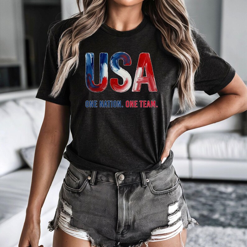 K&ouml;nnte beinhalten: Dunkelgraues T-Shirt mit dem Wort "USA" in rot, wei&szlig; und blau. Darunter steht der Text "ONE NATION. ONE TEAM."