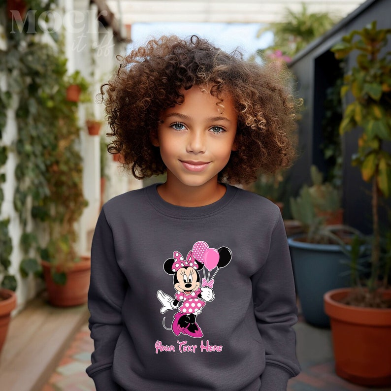 Puede incluir: Una sudadera gris con un gr&aacute;fico rosa de Minnie Mouse sosteniendo globos rosas. El texto "Your Text Here" est&aacute; impreso debajo del gr&aacute;fico.