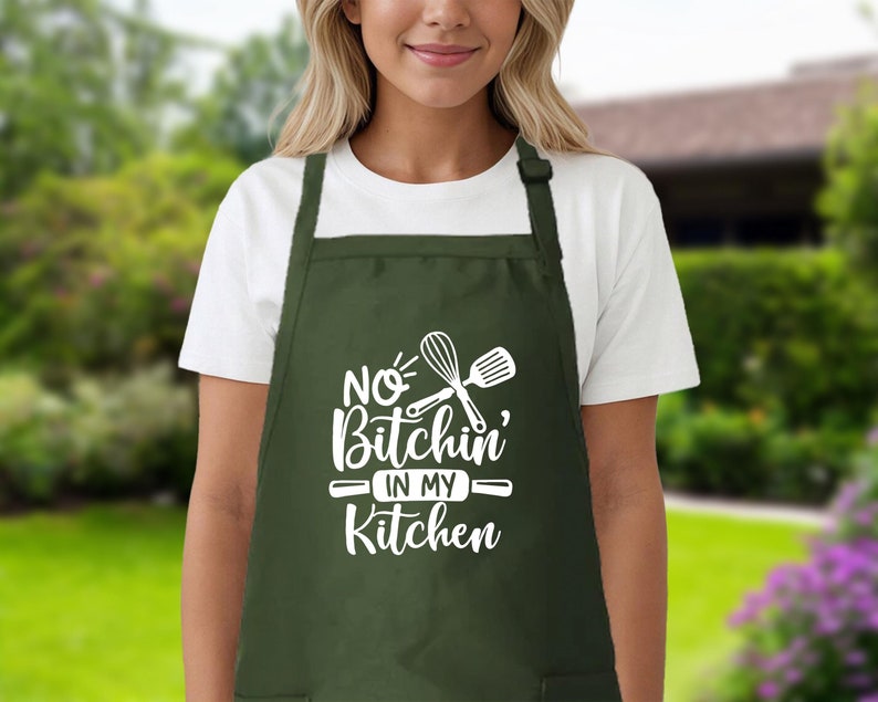 May include: A green apron with white text that says "No Bitchin' in my Kitchen" and a white graphic of a whisk and spatula.