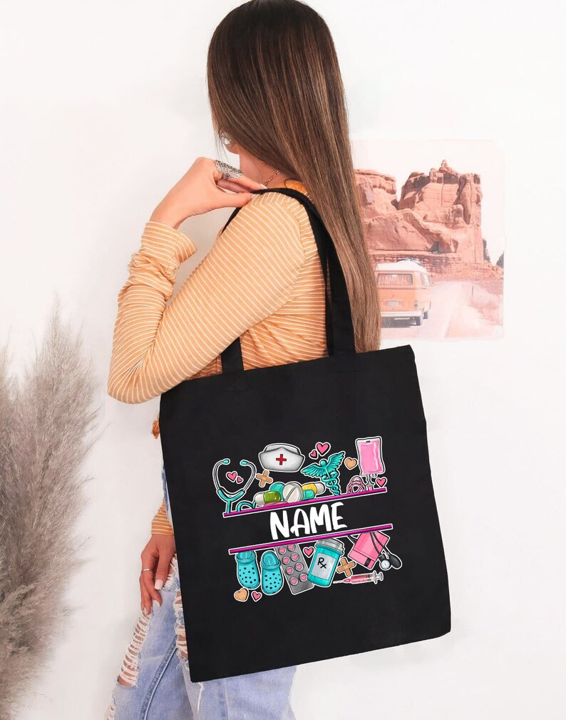 May include: Black tote bag with a colorful design of medical symbols and the word "NAME" in the center. The design includes a stethoscope, pills, a syringe, a bandage, and a heart.