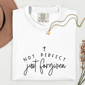 May include: White t-shirt with the text "NOT PERFECT just FORGIVEN" in black script. A gold star pendant necklace and a brown hat are also visible. The shirt has a Comfort Colors tag.