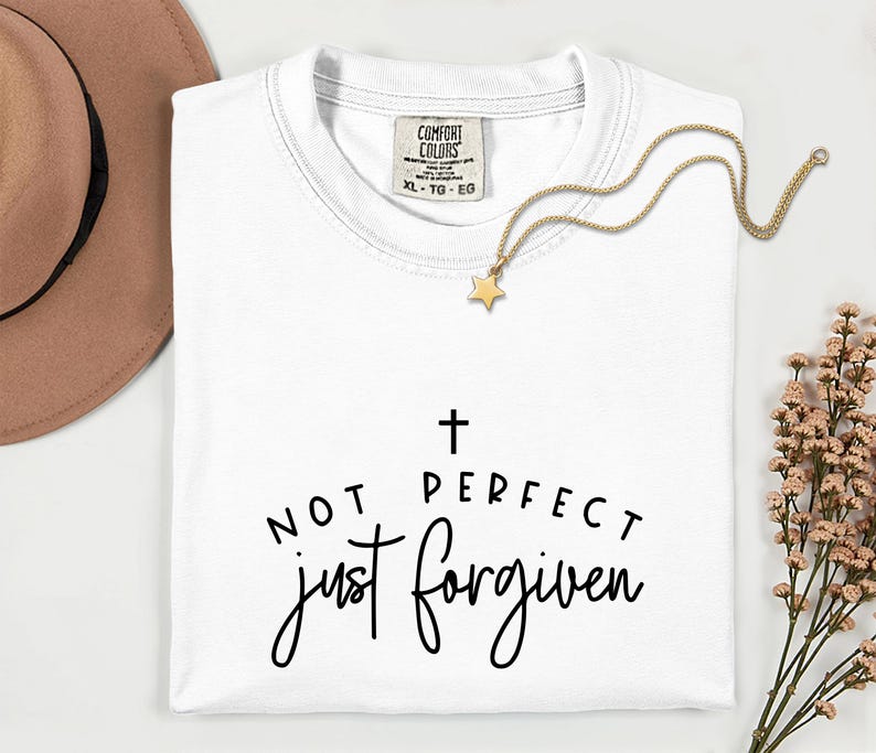 May include: White t-shirt with the text "NOT PERFECT just FORGIVEN" in black script. A gold star pendant necklace and a brown hat are also visible. The shirt has a Comfort Colors tag.