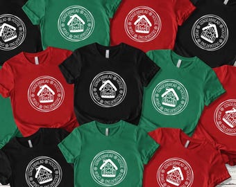 May include: A collection of short-sleeved t-shirts in various colors, including black, red, and green. Each shirt features a white circular graphic with a gingerbread house design and the text "GINGERBREAD HOUSE DECORATING CREW".