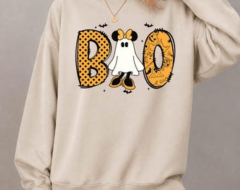 May include: A beige crewneck sweatshirt featuring a graphic print of the word BOO. The letter B is orange with black polka dots, and the letter O contains orange Halloween patterns. A white ghost with a yellow polka dot bow sits in the center.