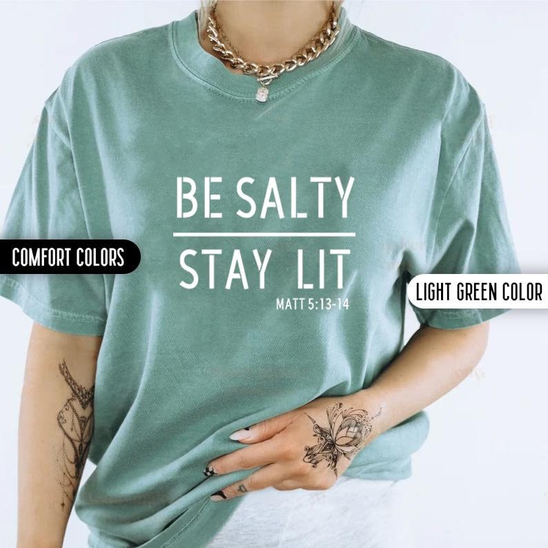 May include: A light green t-shirt with the text "BE SALTY STAY LIT" and the scripture reference "MATT 5:13-14" printed in white.