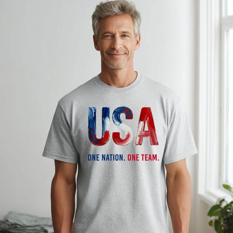K&ouml;nnte beinhalten: Ein graues T-Shirt mit dem Wort "USA" in rot, wei&szlig; und blau. Darunter steht der Text "ONE NATION. ONE TEAM."
