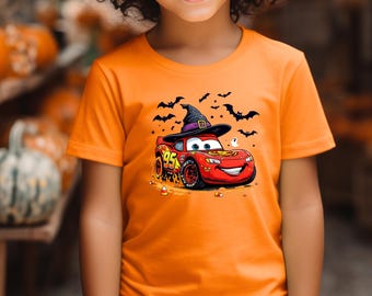 May include: An orange short-sleeved t-shirt featuring a graphic of a red race car with the number 95, wearing a black witch hat. The design includes black silhouettes of flying bats, a small white ghost, and scattered orange and white candy corn.