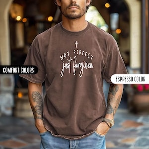May include: Espresso-colored t-shirt with the text "NOT PERFECT just forgiven" in white script and a small cross above the words. The shirt has a crew neck and short sleeves. The shirt is a comfort color.