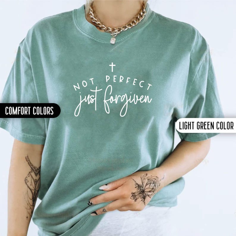 May include: Light green t-shirt with the text "NOT PERFECT just forgiven" in white script. The shirt has short sleeves and a crew neck. The words "COMFORT COLORS" and "LIGHT GREEN COLOR" are printed on the shirt.