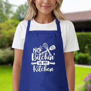 May include: Blue kitchen apron with white text that reads "No Bitchin' in my Kitchen" and a white silhouette of a rolling pin and whisk.