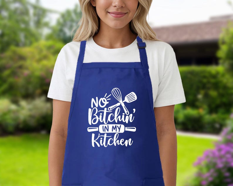 May include: Blue kitchen apron with white text that reads "No Bitchin' in my Kitchen" and a white silhouette of a rolling pin and whisk.
