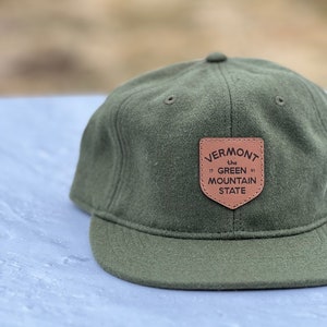 May include: A green baseball cap with a brown leather patch that says "Vermont the Green Mountain State".