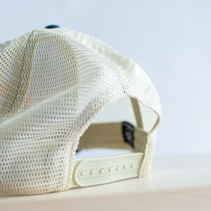 May include: A beige mesh baseball cap with a plastic adjustable strap. The cap is turned inside out, showing the mesh lining.