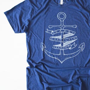 May include: A blue t-shirt with a white anchor graphic. The anchor is surrounded by a banner that reads "LAKE CHAMPLAIN VERMONT".
