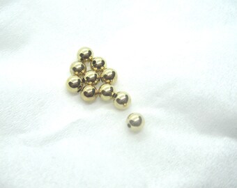 May include: A collection of small, shiny, golden spheres arranged in a cluster on a soft, white fabric. The spheres are reflective, catching the light and creating highlights. The arrangement suggests a decorative or artistic purpose.