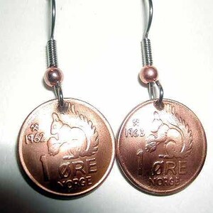 May include: A pair of handmade earrings featuring Norwegian 1 øre coins from 1962 and 1963. The copper-colored coins display a squirrel design and the text "1 ØRE NORGE". Each earring has a silver-tone hook, a copper-colored bead, and a coiled wire detail.