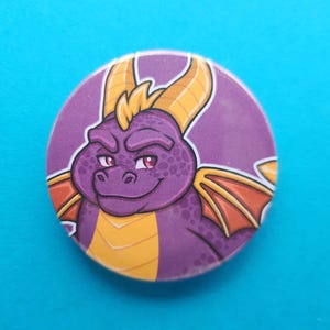 May include: Purple dragon character with yellow horns and wings, smiling with a mischievous expression. The dragon is cartoon-style and has a textured purple body.
